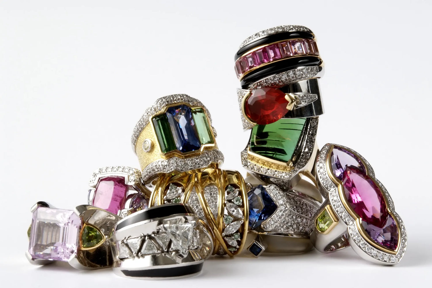 Luxury cocktail ring collection stacked together featuring colorful gemstones including sapphire, emerald, ruby, amethyst, and pink tourmaline set in gold and silver with diamond pavé accents